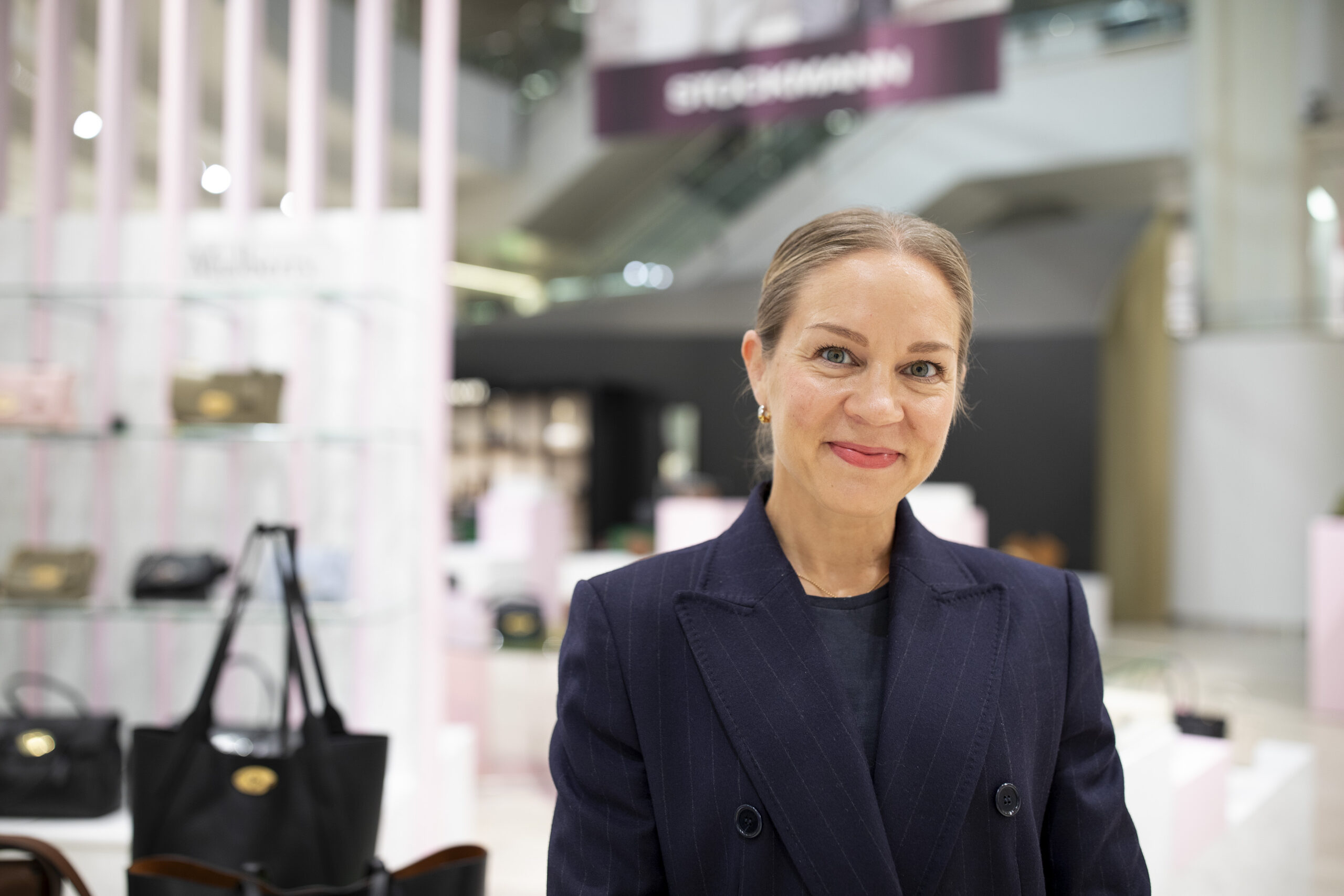 hymyilevä nainen mustassa takissa tavaratalon sisätiloissa